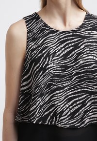 Top senza maniche in bianco e nero con motivo a onde, realizzato in tessuto morbido con vestibilità ampia e scollo rotondo.