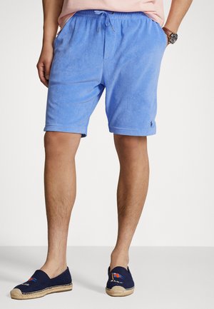 Lyseblå frottéshorts med elastisk midje, sidelommer og en liten logo på nederste kant, kombinert med marineblå espadrillos.