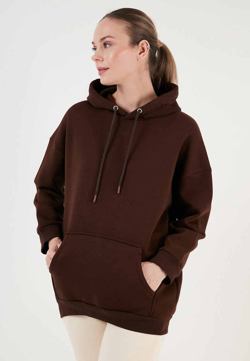 Barna kapucnis sweatshirt elülső zsebből, húzózsinórral és bordázott mandzsettákkal. Puha anyagból készült, laza, oversized szabással.