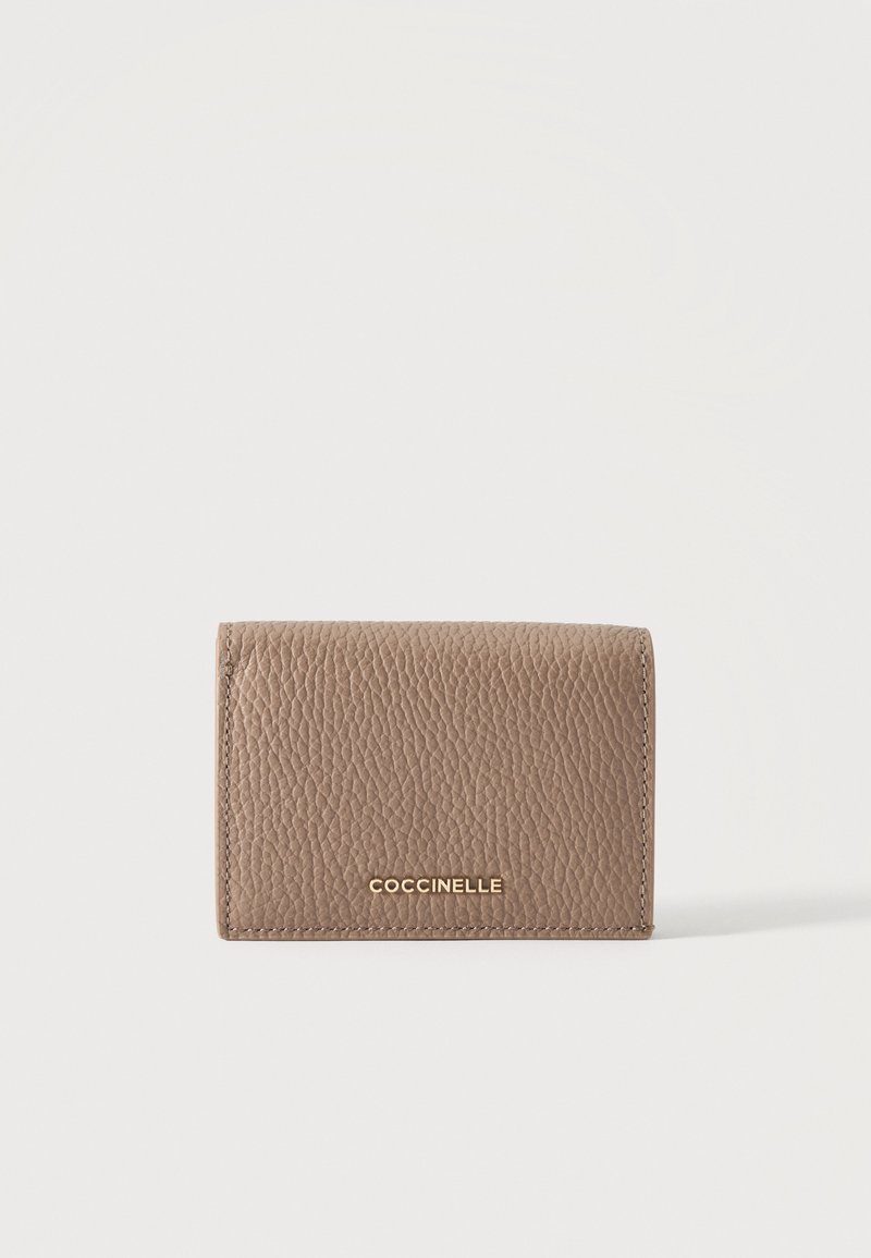 Petit portefeuille en cuir texturé taupe avec logo COCCINELLE doré centré sur le rabat avant sur fond blanc.