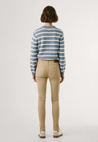 Črtast modro-bele pletene pulover s rebrastimi manšetami, v kombinaciji s bež prilegajočimi kavbojkami z zadnjimi žepi in belimi superge s kremnimi detajli.