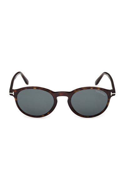 Occhiali da sole con lenti scure rotonde, montatura tartarugata e aste sottili, con un piccolo dettaglio a "T" argentato vicino alle cerniere.