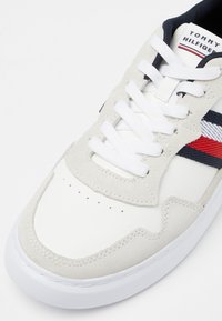 Sneaker bianco con tomaia in suede e pelle. Caratterizzato da lacci bianchi, punta testurizzata e dettagli a righe rosse e blu sui lati.