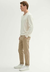 Light beige pullover with a collar, beige tapered pants, and white sneakers. Smooth texture and casual design. Neutral color palette.