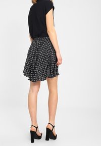 Falda negra con diseño blanco estampado, de forma acampanada y material ligero; combinada con una blusa negra y tacones negros.