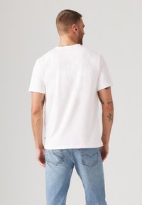 Witte katoenen t-shirt met korte mouwen en een ronde hals. Glad textuur en een ontspannen pasvorm, gecombineerd met lichtblauwe denim jeans.