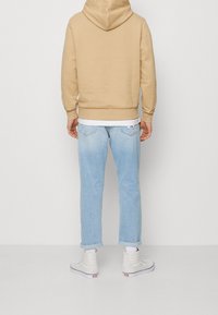 Felpa khaki con tasca a marsupio, abbinata a jeans blu chiaro. Sneakers bianche alte completano l'outfit. Visuale posteriore mostrata.