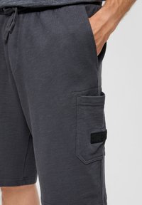 Shorts gris foncé en mélange de coton doux, avec une taille élastique, des poches latérales et une grande poche à patch arborant un accent logo noir.