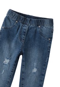 Jeans de mezclilla azul con cintura elástica y parches desgastados en los muslos delanteros, que cuentan con bolsillos frontales y remaches metálicos.