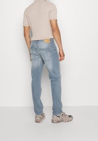 Jeans in denim blu chiaro con una vestibilità dritta, texture sbiadita e tasche posteriori. Indossati con una maglietta a maniche corte in maglia e sneakers.