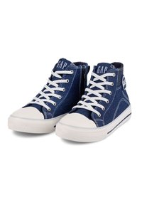 Zapatillas altas de mezclilla en azul oscuro con punteras y suelas de goma blanca. Cuenta con cordones blancos y el logo de GAP en la lengua y en el lateral.