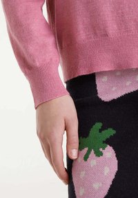 Suéter de cashmere rosa claro con puños acanalados, combinado con una falda negra con un patrón de fresas rosas y lunares blancos.
