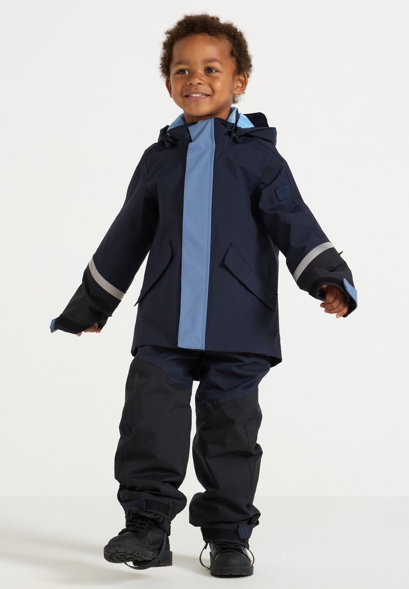 Navy waterproof jacket with light blue accents and reflective stripes, paired with matching pants and black boots, designed for children.