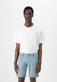 Hvid T-shirt med korte ærmer, parret med lyseblå denimshorts. Shortsene har opfoldede manchetter og frontlommer med knaplukning.