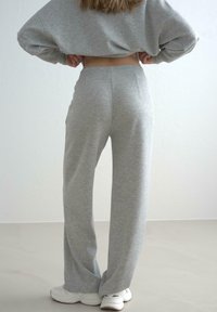 Grå sweatpants lavet af blødt stof, der har en afslappet pasform, elastisk talje og en subtil meleret tekstur, parret med hvide sneakers.