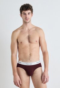 Burgundi Calvin Klein alsónadrág fehér logós derékrésszel, sima, rugalmas anyagból, klasszikus alsónadrág szabással készült.