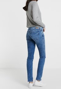 Prudké modré denimové džíny s mírně zvýšeným pasem, jemným prošlapáním, pěti kapsami a koženou značkovou nášivkou na zadním pásu.