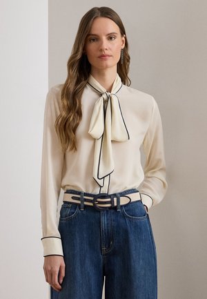 Kreemikas pluus musta ääristusega, kaelas lipsudetailiga, kombineeritud kõrge vöökohaga siniste teksapükstega ja beež vöö ringikujulise pandlaga.