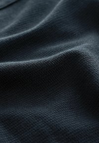 Dark fabric with a textured weave, showing ripples and folds. The color is a deep navy or black, emphasizing depth and material detail.