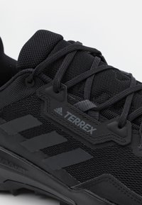 Czarne buty trekkingowe z siateczkową cholewką, teksturowanymi akcentami i logo "Terrex". Zawierają czarne sznurowadła i wytrzymały wzór podeszwy.