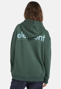 Grön hoodie med en avslappnad passform, med en framfickor av typ känguru, ribbade ärmslut och en stor textlogotyp på baksidan i ljusblått.