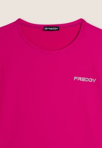 Camiseta de manga corta fucsia, hecha de una tela suave, con un escote redondo y el logo plateado "FREDDY" en el lado izquierdo.