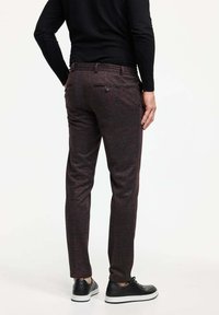 Dunkelbraune Hose mit dezentem Muster, schlanker Schnitt, seitliche und hintere Taschen, kombiniert mit schwarzen Sneakern, getragen von einer Person von hinten.