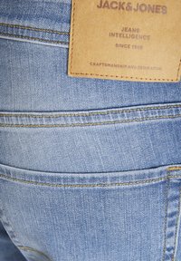 Jeans de mezclilla azul claro con costuras visibles, una etiqueta de cuero que muestra "Jack & Jones" y un diseño estándar de bolsillo trasero.