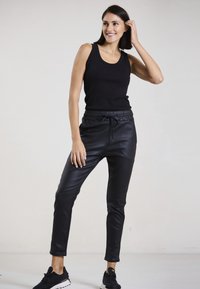Schwarzes geripptes Tanktop und schwarze jogger aus Kunstleder mit elastischem Bund und Kordelzug. Legere Sneakers vervollständigen den Look.