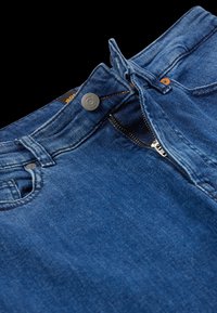 Jeans de mezclilla azul oscuro con cierre de botón y cremallera. Presentan bolsillos cosidos y una textura suave. Diseño de tiro medio con trabillas para cinturón.