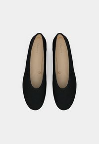 Een paar zwarte Calvin Klein balletschoenen met een beige interieur, van bovenaf bekeken op een witte achtergrond.