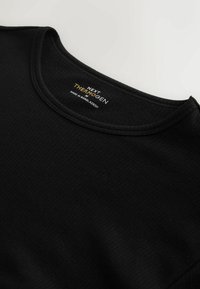 Čierne pruhované tričko s dlhými rukávmi a okrúhlym výstrihom. Štítok zobrazuje nápis "NEXT THERMOGEN M" a "VYROBENÉ V BANGLADÉŠI." Mäkká textúra.