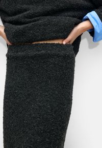 Czarny, fakturowany sweter i spódnica, uszyte z miękkiego, puszystego materiału, z surowym wykończeniem dekoltu i w talii, oraz niebieskim akcentem pod spodem.