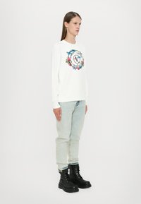 Felpa bianca con stampa floreale e di farfalle in colori vivaci, abbinata a jeans di denim chiaro e stivali militari neri con lacci.