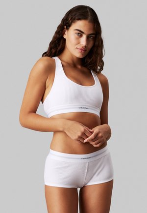 Hvit ribbet sports-bh med brede stropper og signaturlogo-bånd, parret med matchende ribbet boyshorts med et lignende logo-bånd.