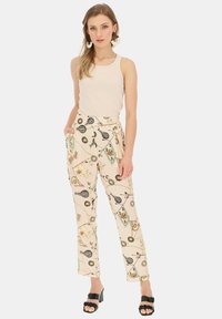 Spodnie w kolorze kremowym z nadrukiem w różnorodne kolorowe motywy, wysoki stan, kieszenie boczne i prosta nogawka. Noszone z dopasowanym topem na ramiączkach i czarnymi sandałami.