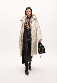 Lång, ljusbeige quiltad pufferjacka; djurmönstrad topp; svart läderkjol med knappdetaljer; svarta klackboots; liten strukturerad handväska.