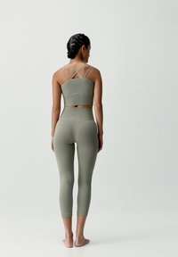 Oliwkowy dopasowany stanik sportowy z krzyżującymi się ramiączkami i pasującymi legginsami z wysokim stanem, z teksturowanym żeberkowym wzorem.