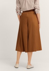 Braune Culottes mit glatter Textur, weitem Bein-Design und hohem Taillenbund. Getragen mit einem gestreiften Hemd und hellen Schuhen.