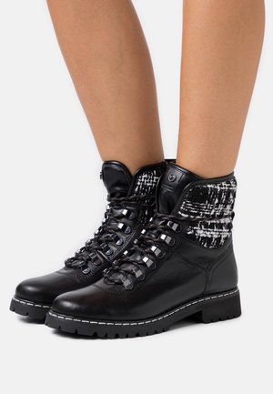 Bottines en cuir noir avec une tige en tissu texturé noir et blanc, dotées d'œillets métalliques, de lacets et d'une semelle robuste avec des coutures blanches.