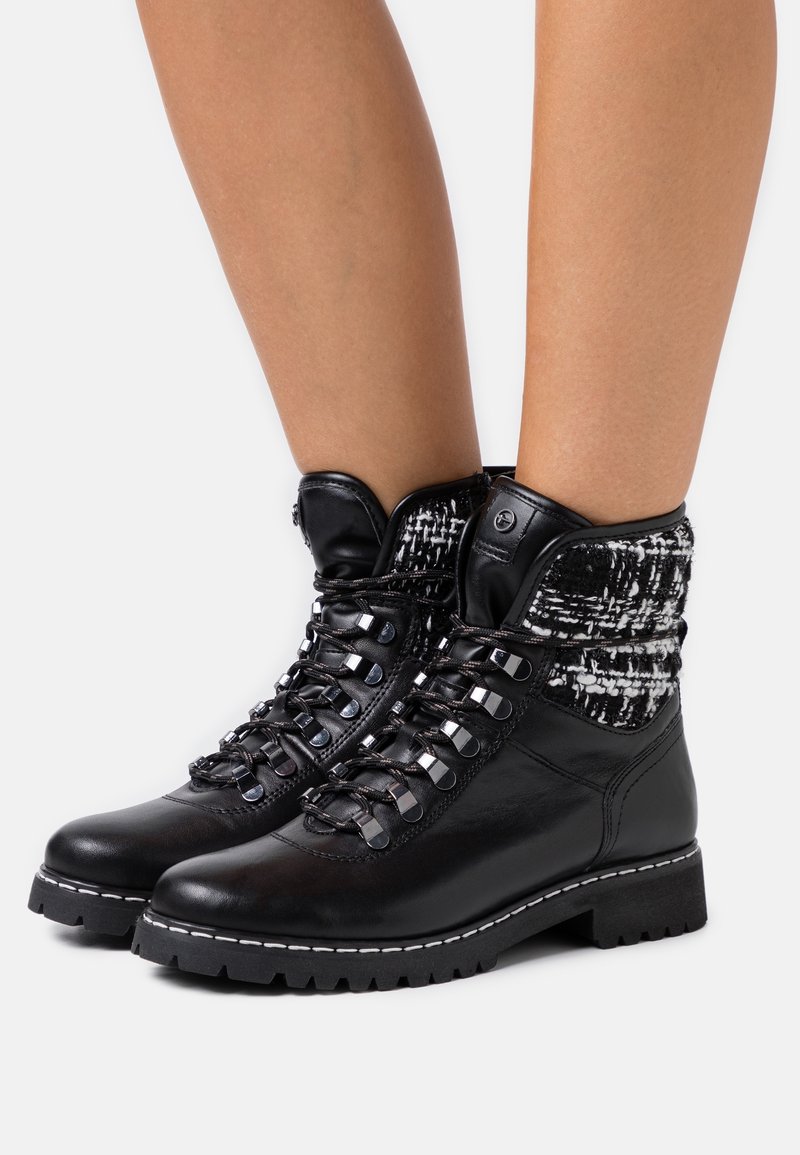 Botas de cuero negras hasta el tobillo con un puño de tela texturada en blanco y negro, que presentan ojales metálicos, cordones y una suela resistente con costuras en blanco.