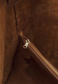 Intérieur en daim marron avec une poche zippée dotée d'une fermeture éclair en métal doré. Texture lisse et détails de coutures contrastantes.