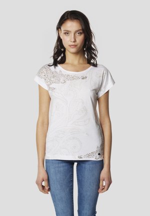 Camiseta blanca de algodón con mangas cortas y cuello redondo; presenta diseños intrincados en tono marrón claro de flores y estampado de leopardo.