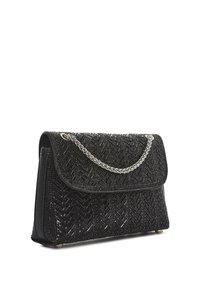 Zwarte geweven clutch met een gestructureerd patroon, klepsluiting en een zilveren kettinghandvat, staand op kleine metalen pootjes.