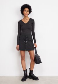 Top nero a maniche lunghe con scollo a V, abbinato a una mini gonna nera con laccatura frontale e due tasche. Stivaletti neri alla caviglia e borsa.