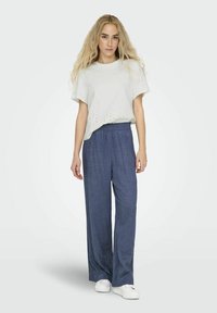 Top gris clair à manches courtes avec des détails en broderie au niveau de l'ourlet, associé à un pantalon bleu marine ample et des baskets blanches.