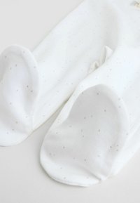 Biele ponožky s malými sivými bodkami; mäkká tkanina; zaoblená špička; hladká textúra; vystlané podrážky; bez viditeľného označenia alebo ozdôb.