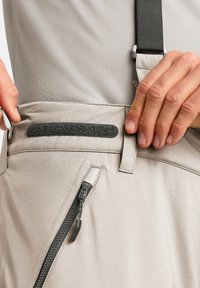 Lichtbeige broek met een soepele textuur, voorzien van een zijrits zak, een zwarte verstelbare band en een klittebandaccent op de tailleband.