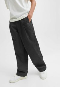 Svarta vida byxor i lätt material, med sidofickor och en avslappnad passform, kombinerat med vita sneakers.