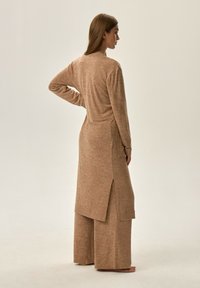 Jasno brązowy dzianinowy strój składający się z długiej bluzki z bocznym rozcięciem i spodni z szerokimi nogawkami. Tekstura jest miękka i lekko puszysta.